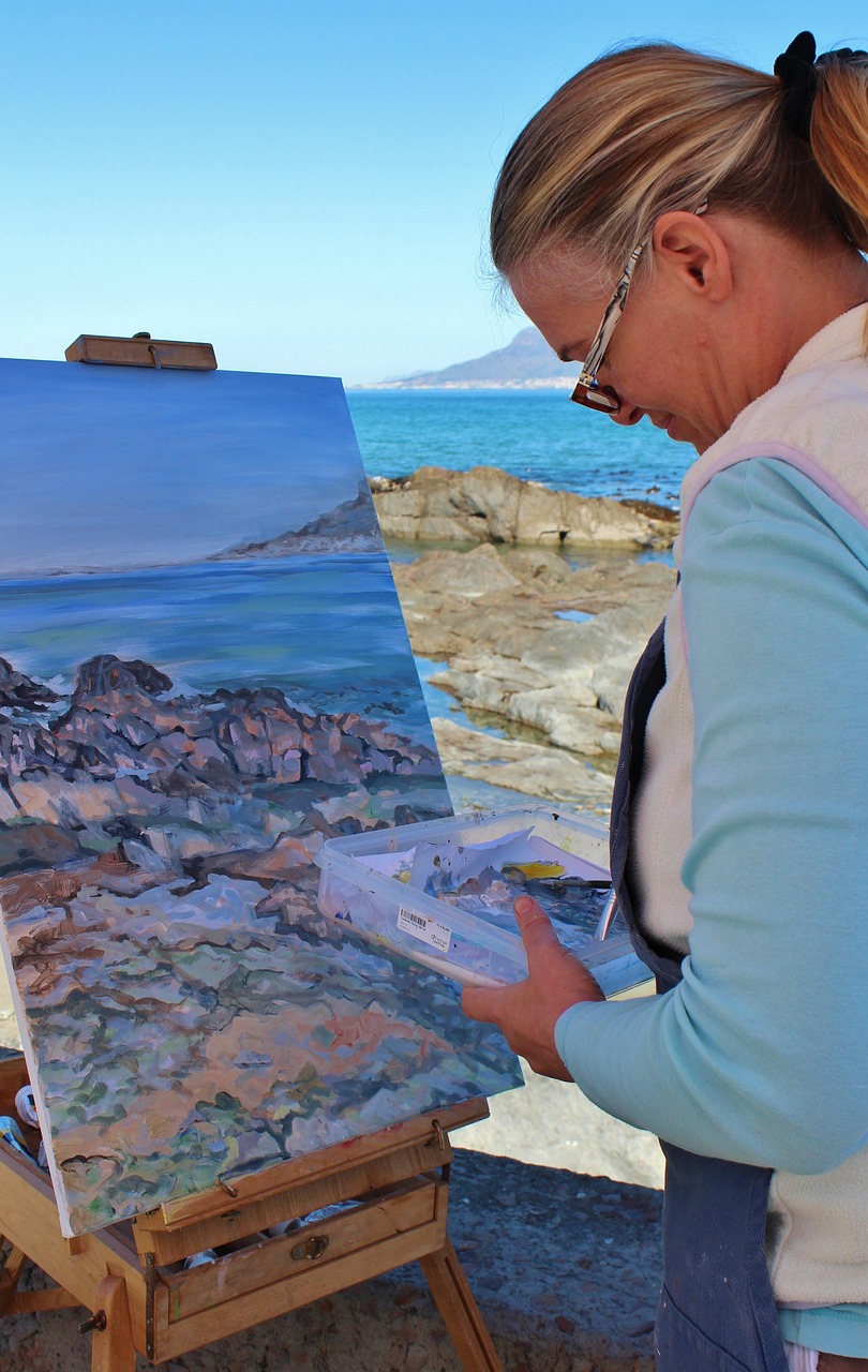 Middle aged woman painting a seascape while standing on a rocky shore