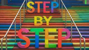 Vibrant rainbow stairs with bold 3D letters spelling “STEP BY STEP,” symbolizing progress, motivation, and personal growth.