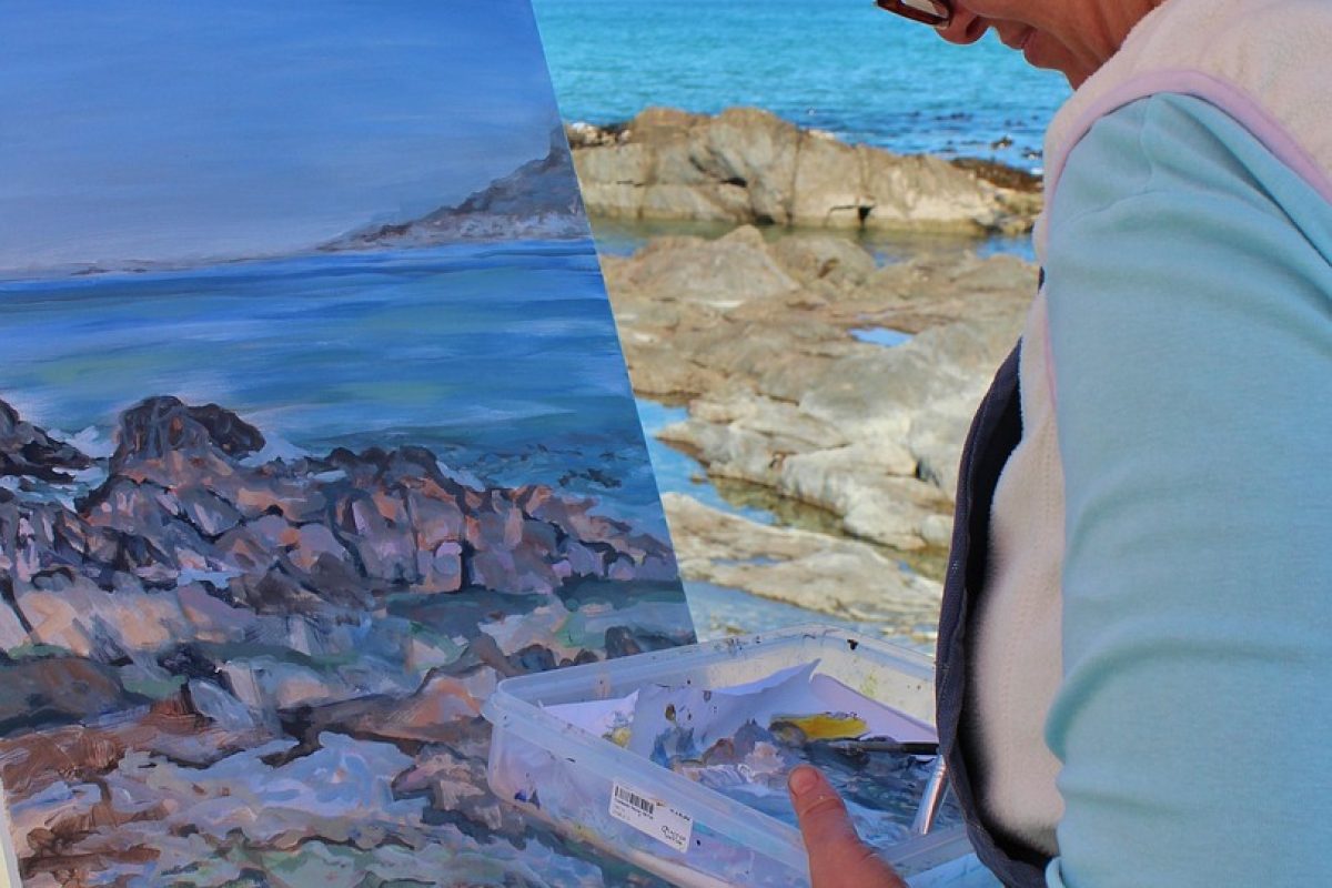 Middle aged woman painting a seascape while standing on a rocky shore